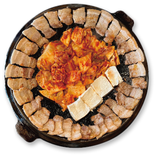 무쇠김치삼겹 — 무쇠 뚜껑 불판 가장자리에 삼겹살을 두르고 가운데 김치와 두부를 올린 모습 (본사 메뉴 사진)