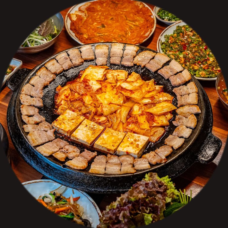 무쇠 불판에 삼겹살을 둘러 굽고 가운데에 볶은 김치와 두부를 올린 한상 — 무쇠김치삼겹 명동점